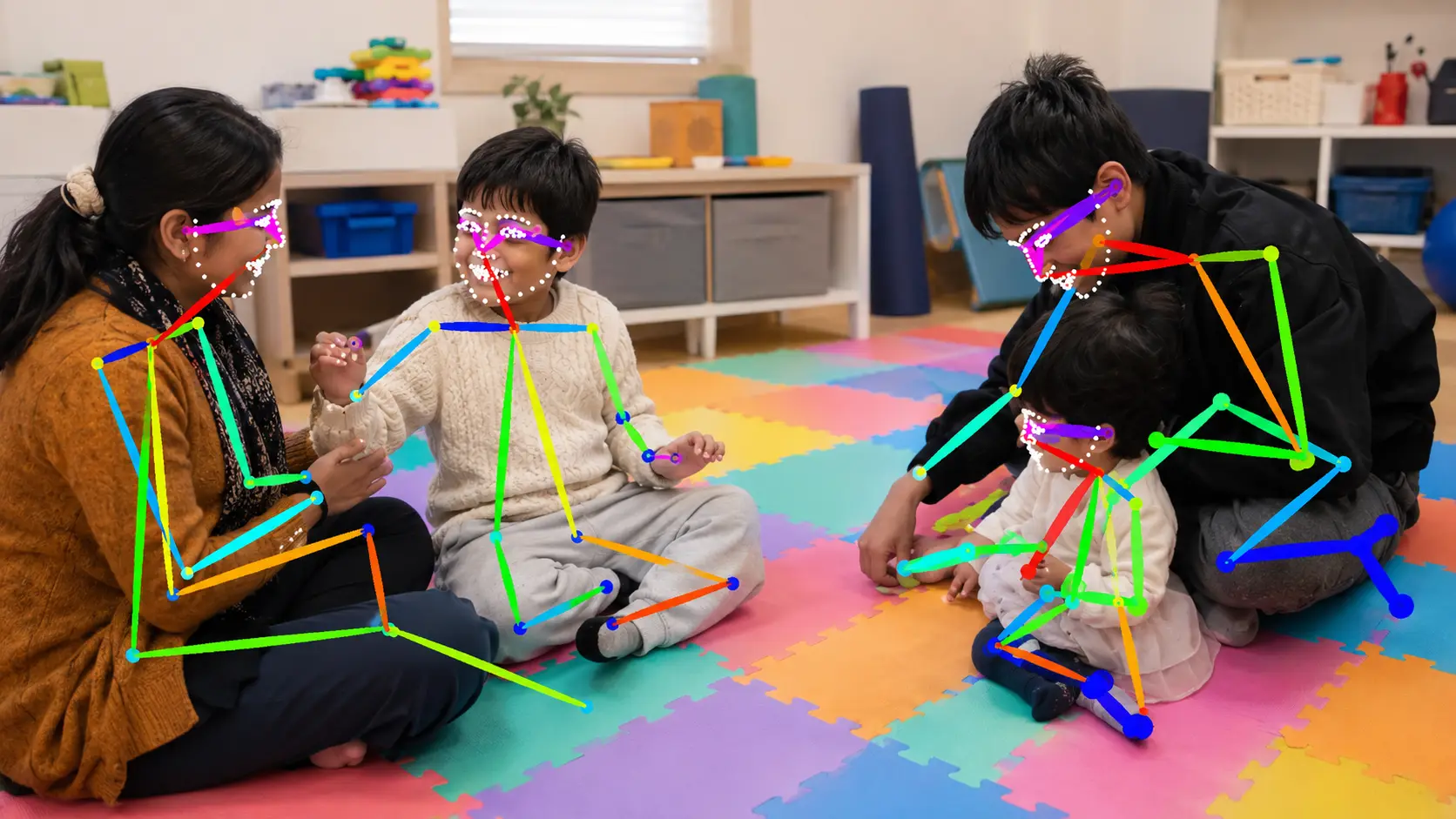 Two therapists playing with two small children on a foam playmat, with coloured skeleton lines drawn over each person by pose-tracking software.