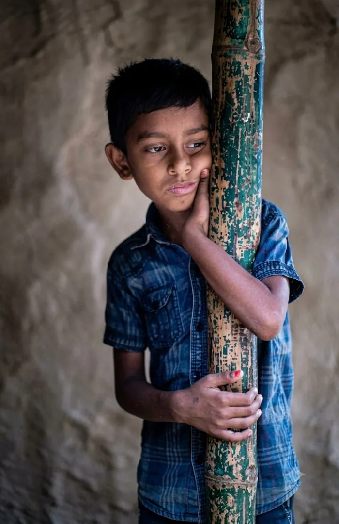 A boy holding a bamboo post, looking away