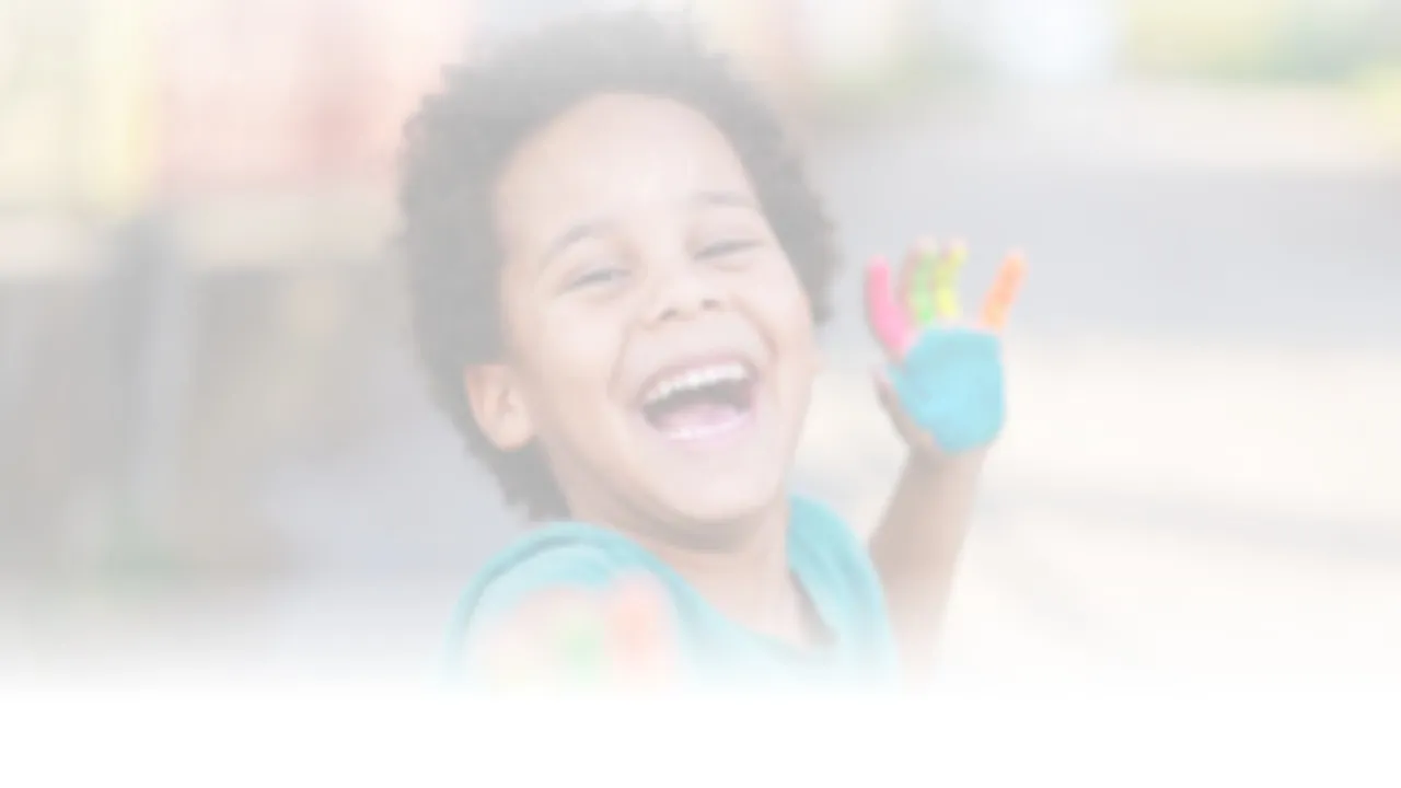 A laughing boy holding up paint-covered hands